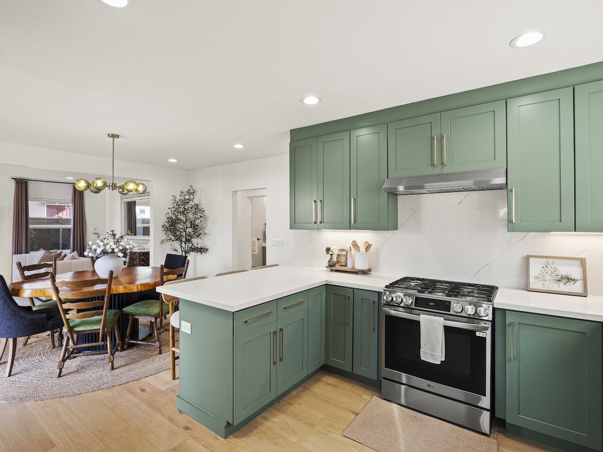 Sage Green Kitchen Cabinet Painting Kitchen with sage green cabinets, brass handles, white countertops, and a stainless steel range beside an open dining area.