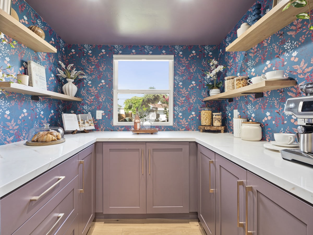 Mauve Pantry Cabinet Painting Pantry with mauve cabinets, brass handles, white countertops, and blue floral wallpaper.