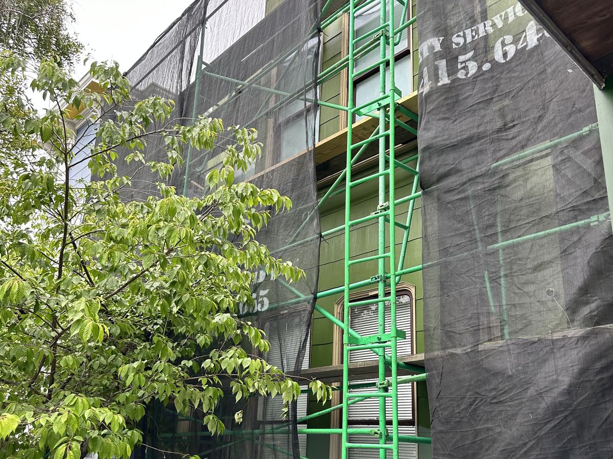 San Francisco Duplex Scaffolding San Francisco duplex with green siding and decorative window trim behind scaffolding and protective mesh.