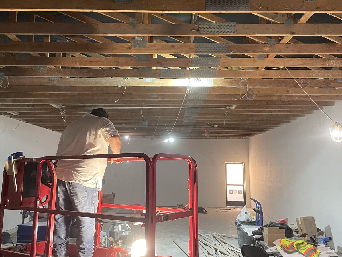 Commercial Interior Lift Work Worker on a red scissor lift beneath exposed wooden ceiling trusses during an interior renovation.
